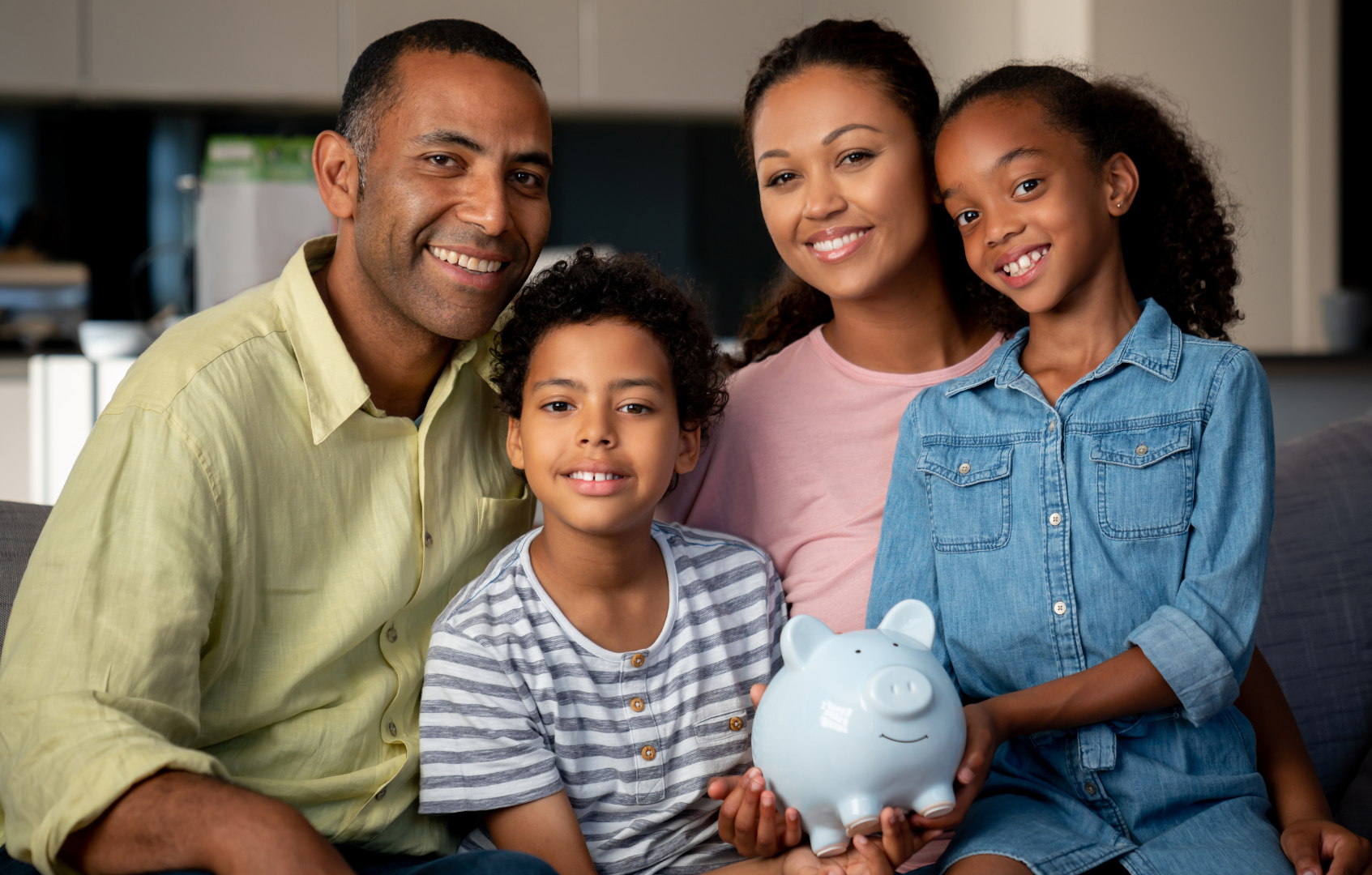 A family is sitting on a couch holding a piggy bank.