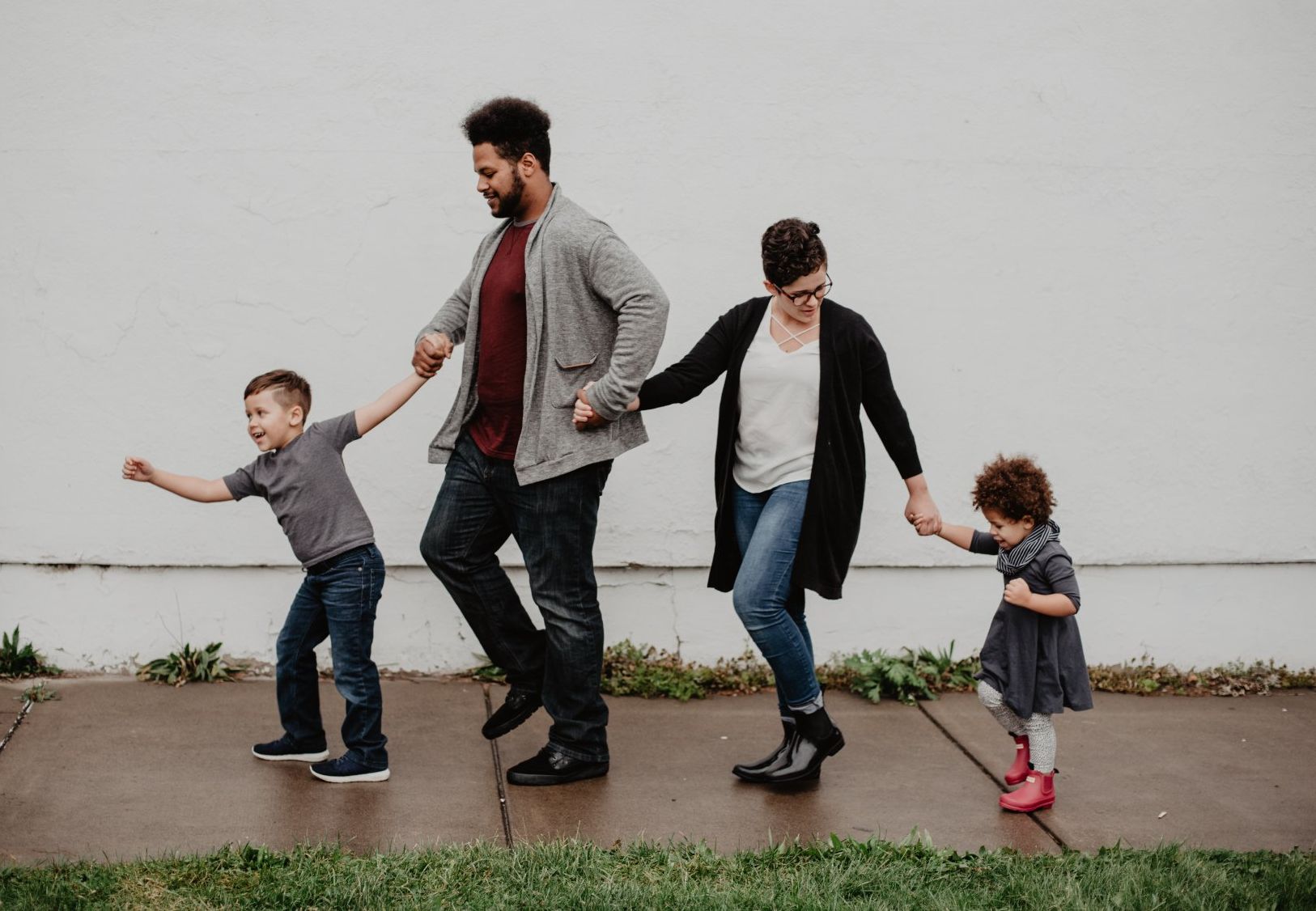 A family is walking down a sidewalk holding hands.