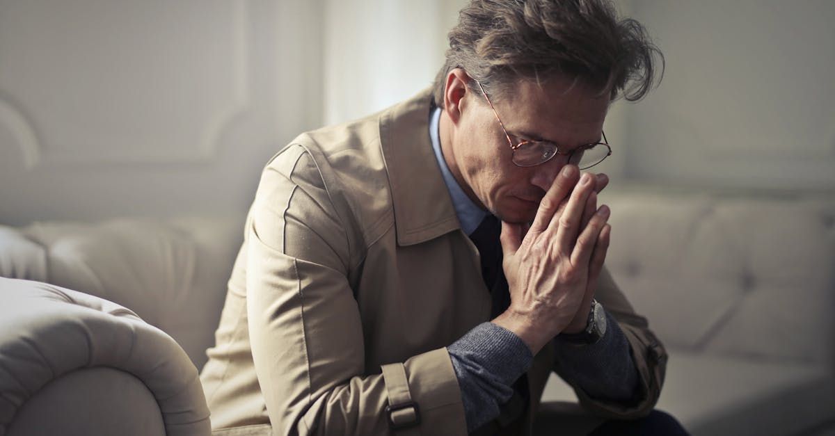 A man is sitting on a couch with his hands folded in prayer.