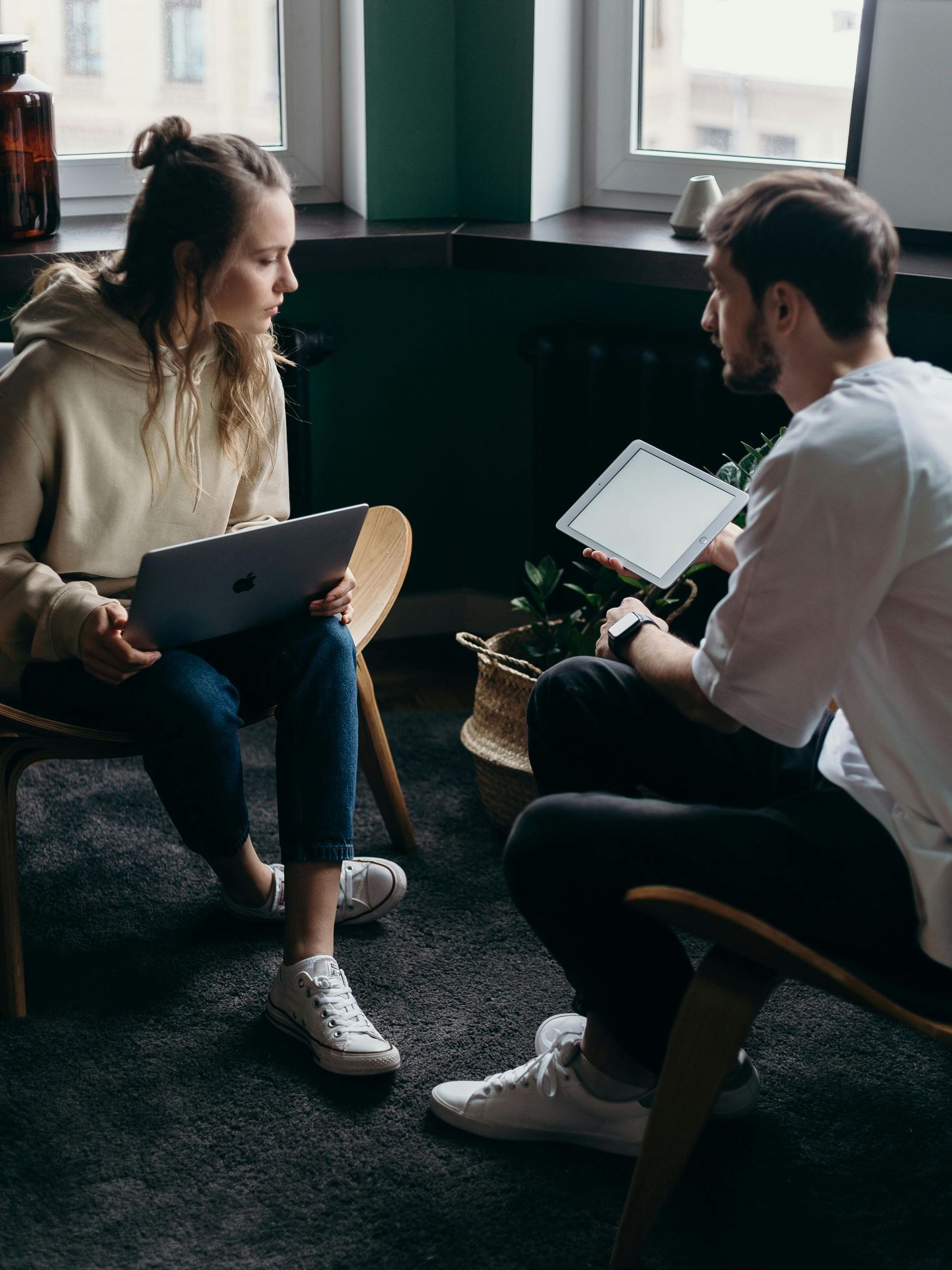 A man and a woman are sitting in chairs looking at a tablet.