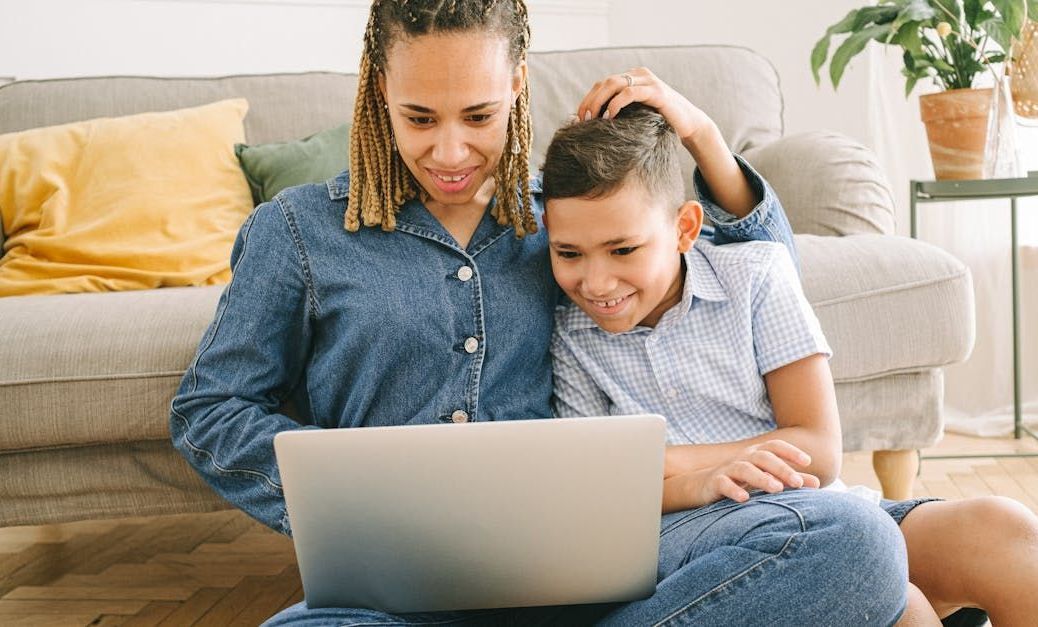 A woman and a child are sitting on the floor using a laptop computer.