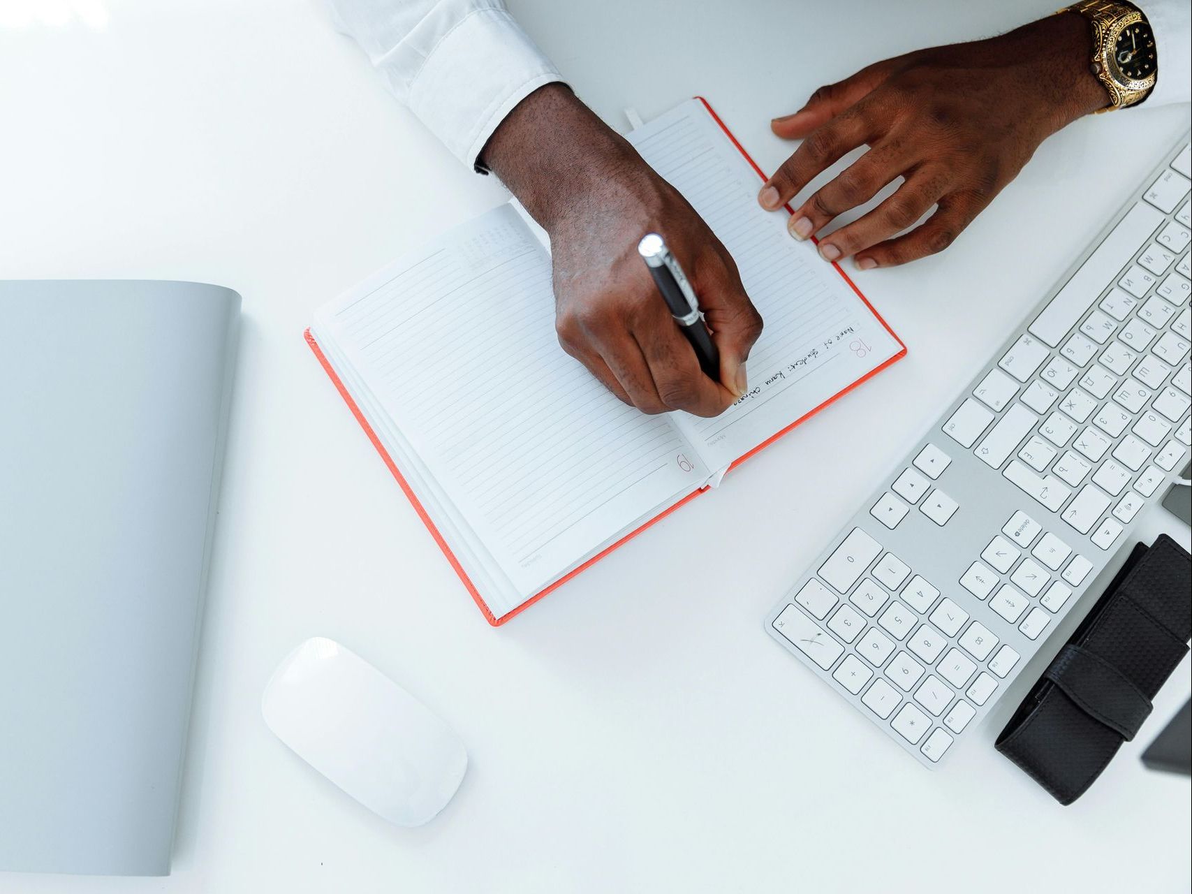 A person is writing in a notebook next to a keyboard.