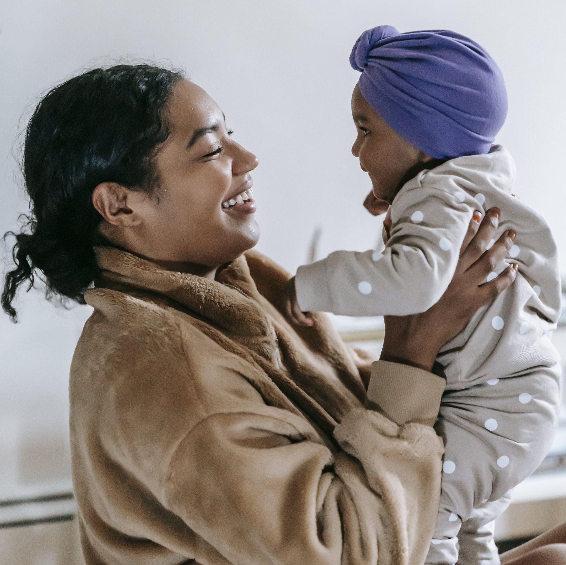 A woman is holding a baby in her arms and the baby is wearing a purple turban.