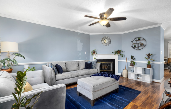 a living room with a couch , ottoman , fireplace and ceiling fan .