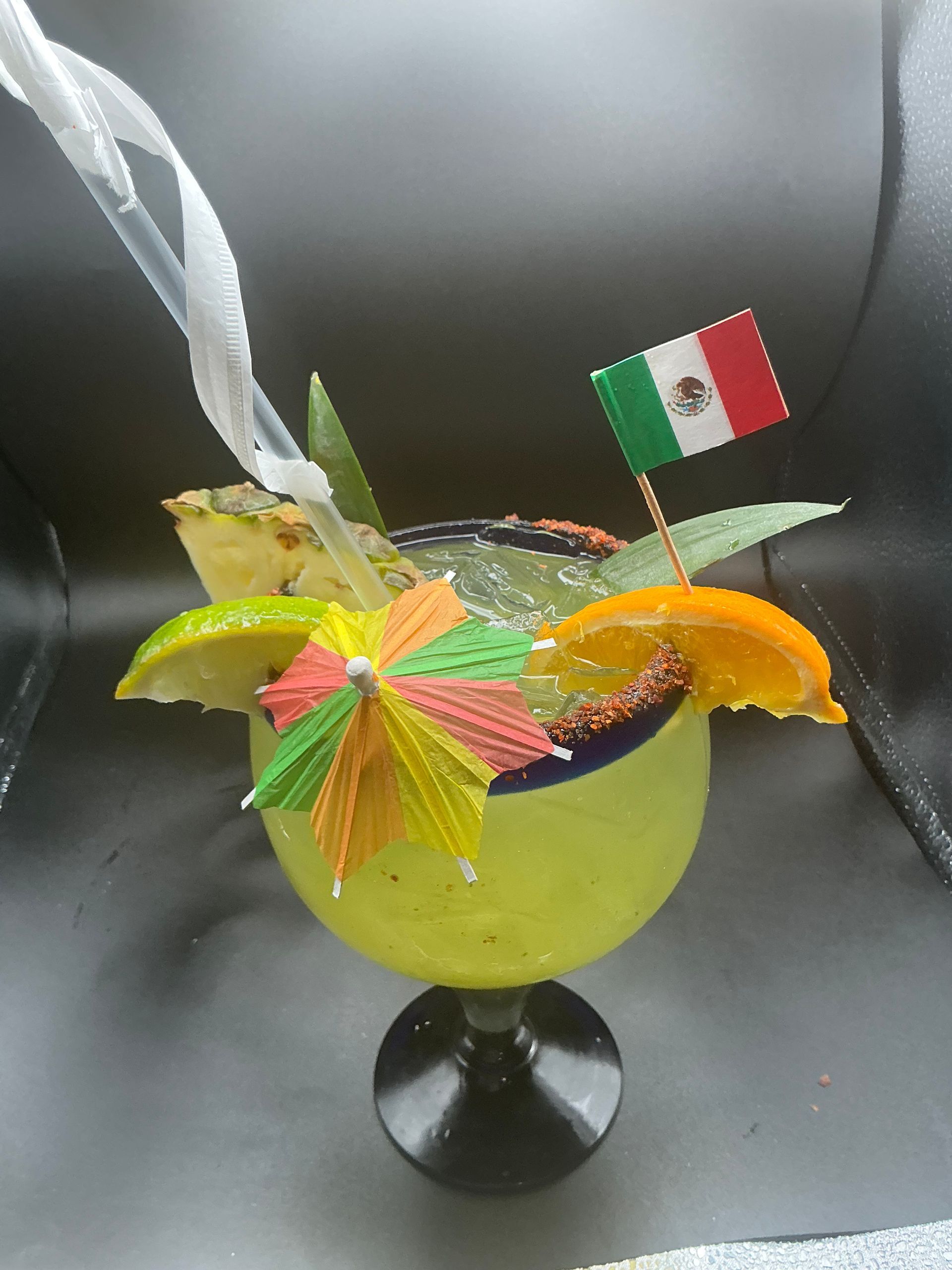 Margarita in a green glass, garnished with fruit, a mini umbrella, and a Mexican flag.
