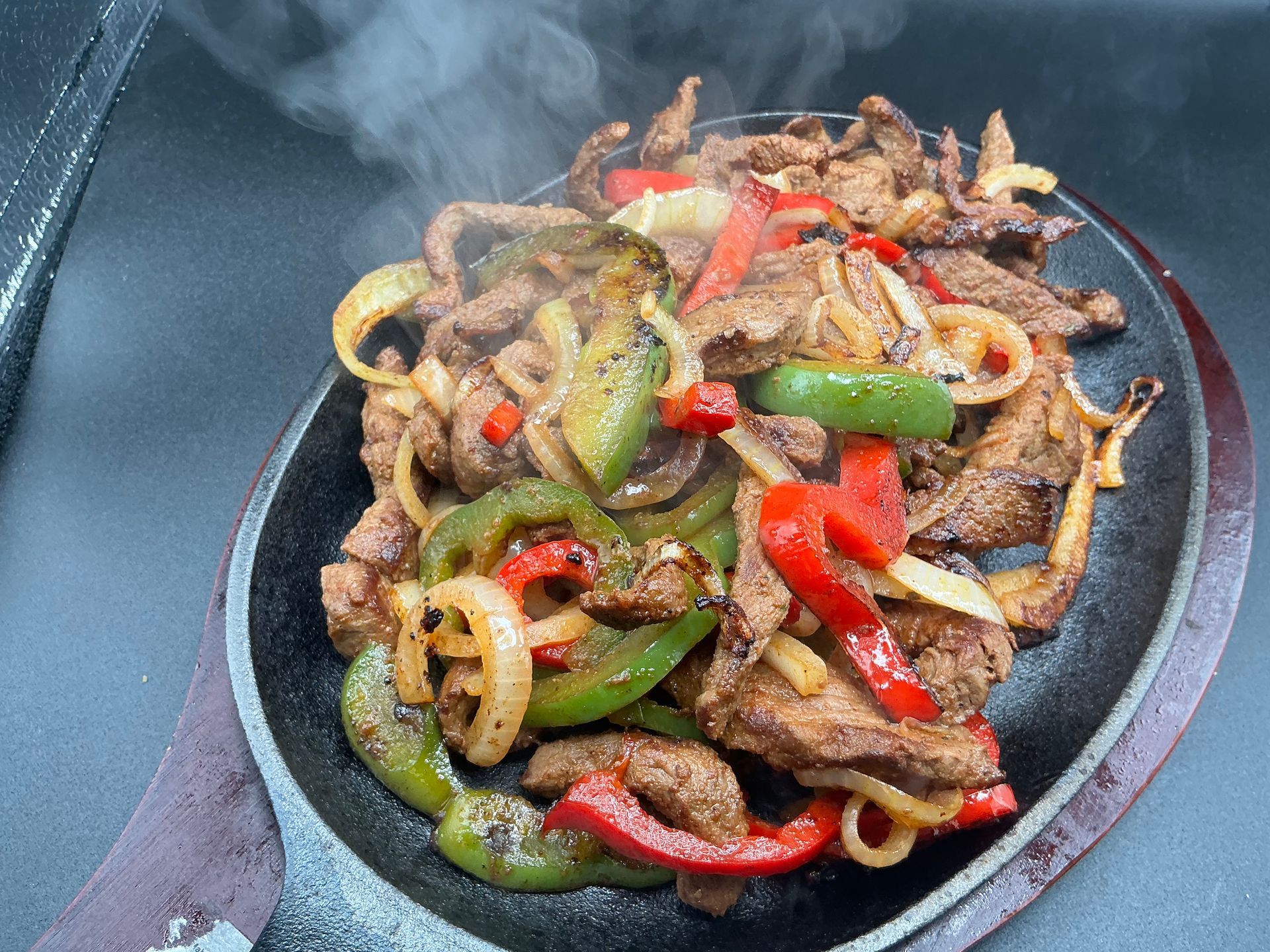 Sizzling fajitas with strips of meat, bell peppers, and onions on a hot, cast-iron plate.