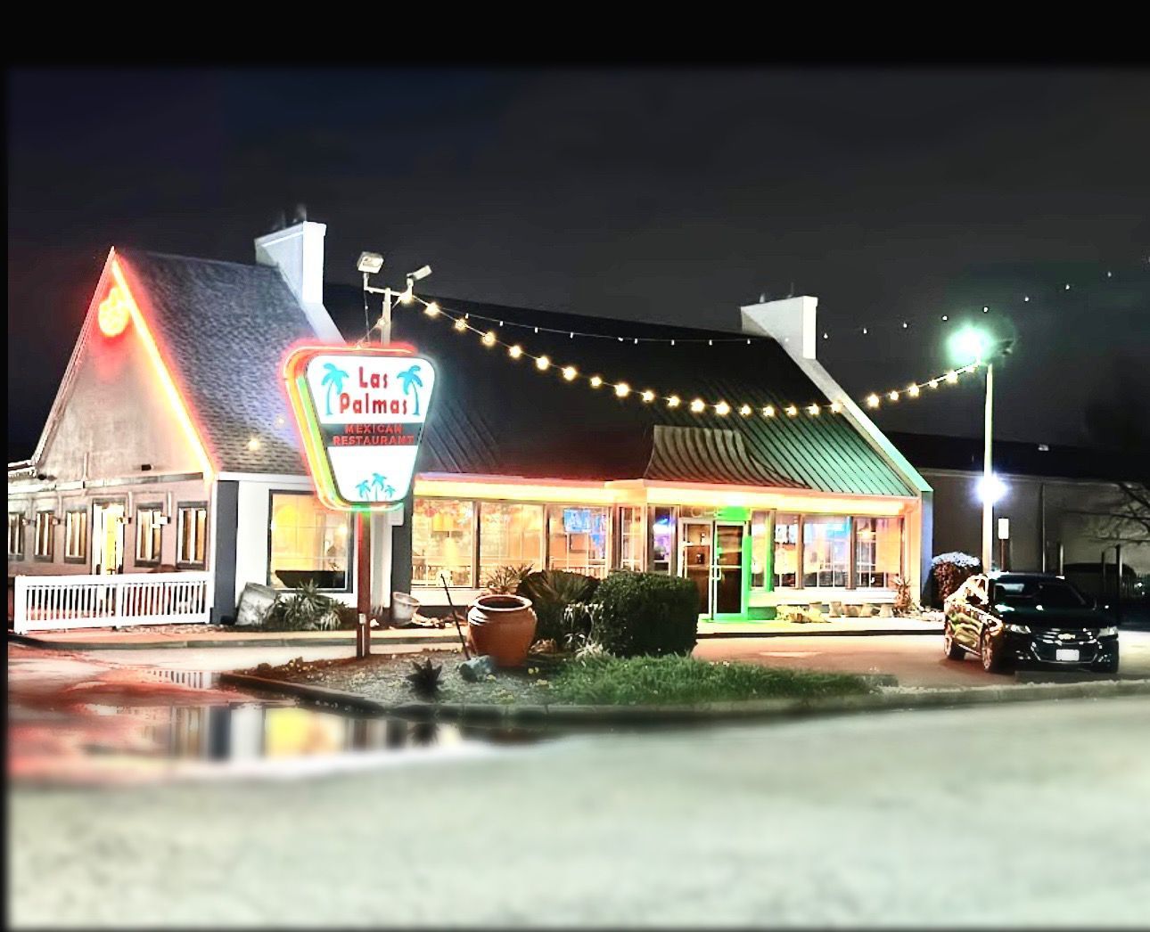 Las Palmas restaurant at night, illuminated sign, string lights, parked car.