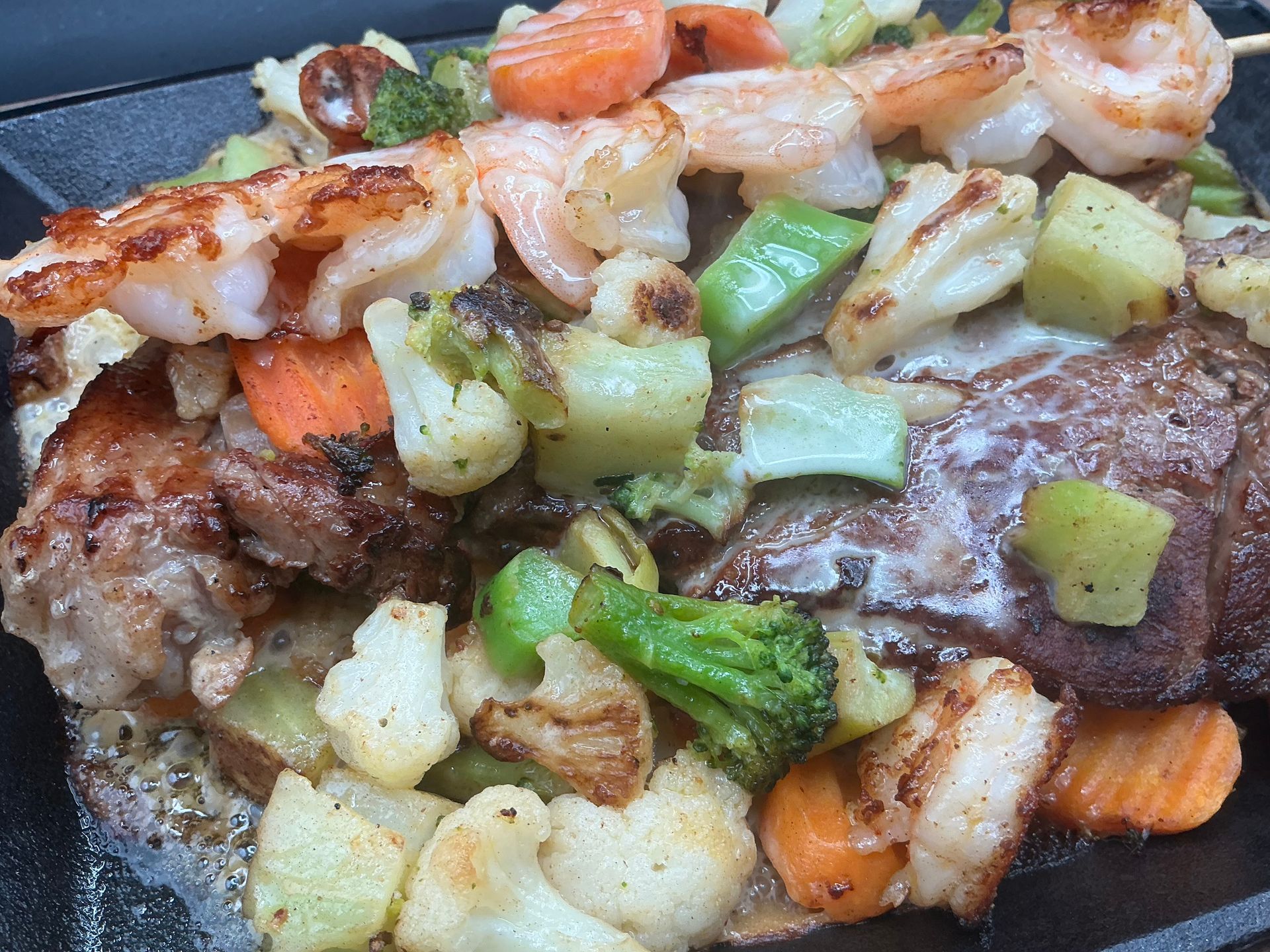 Grilled shrimp skewer over steak, with mixed roasted vegetables.