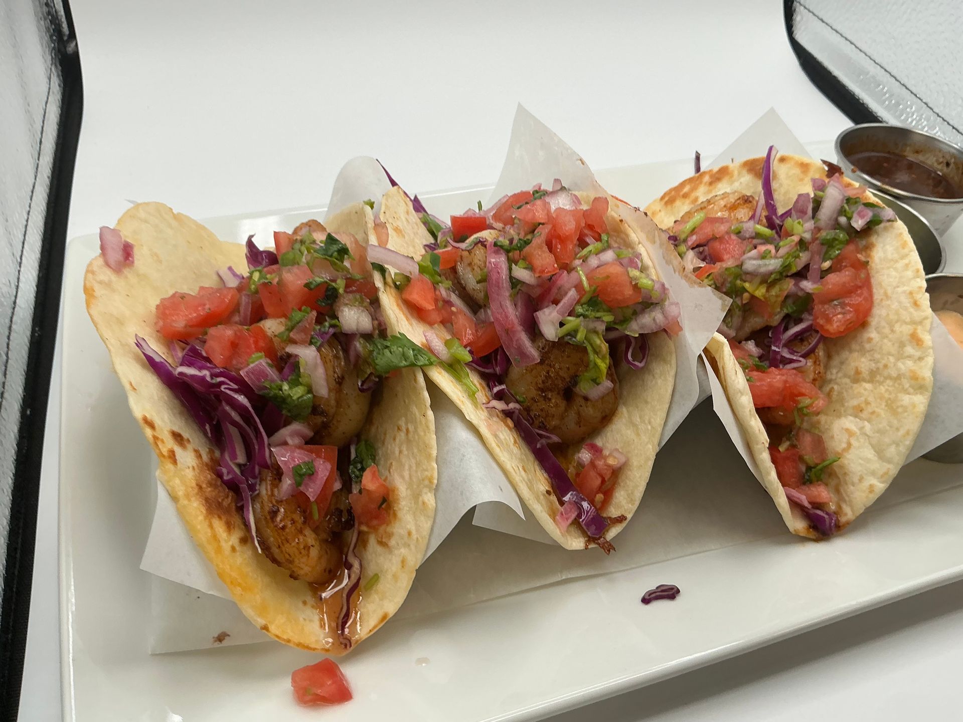 Three shrimp tacos on a white plate, topped with salsa and red cabbage.