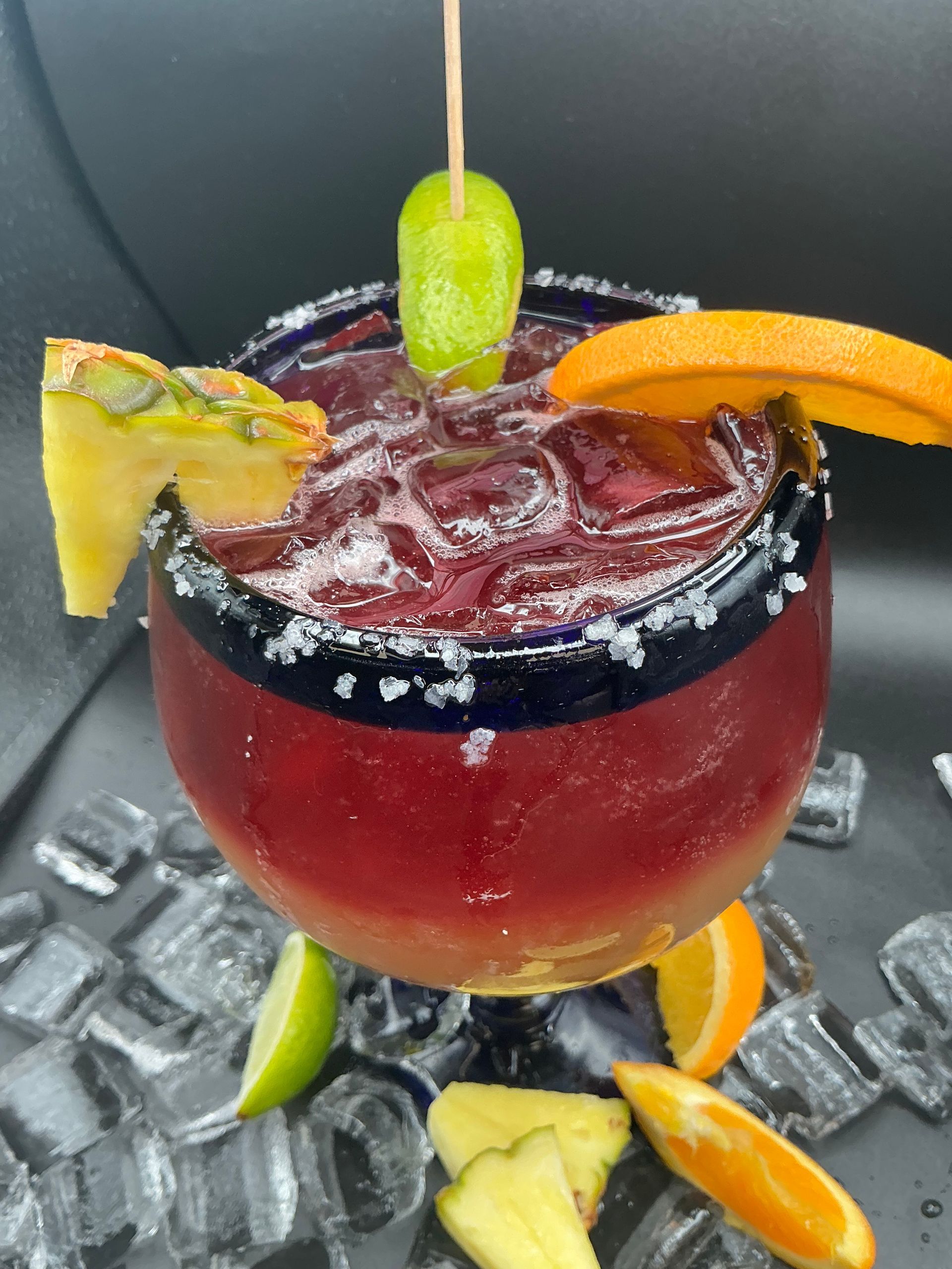 Red cocktail in a glass with a salted rim, garnished with fruit and a lime.