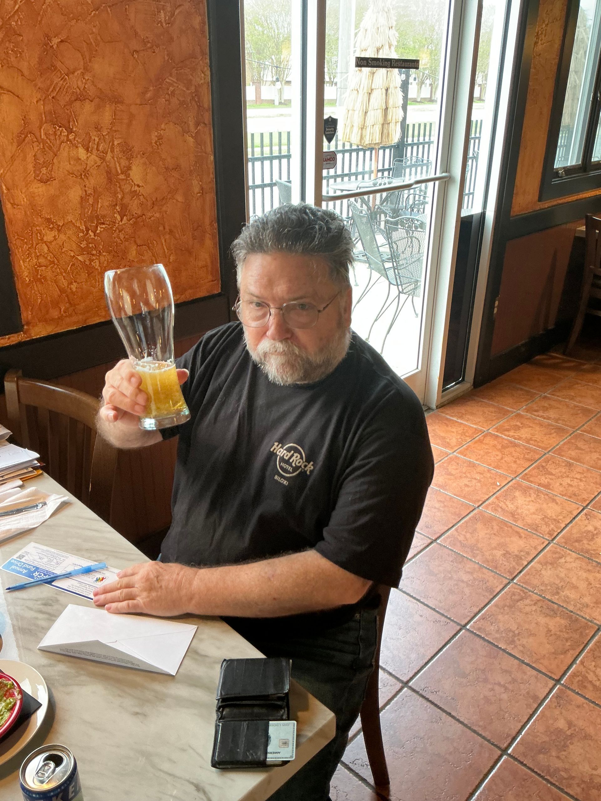 Man holding up a glass of beer, inside a restaurant.