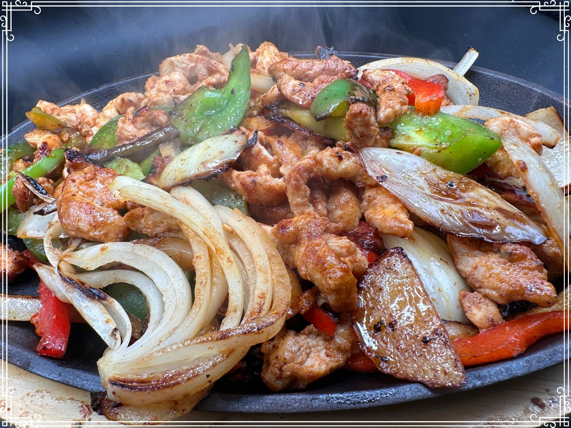Sizzling chicken fajitas with onions and peppers on a hot cast iron plate.