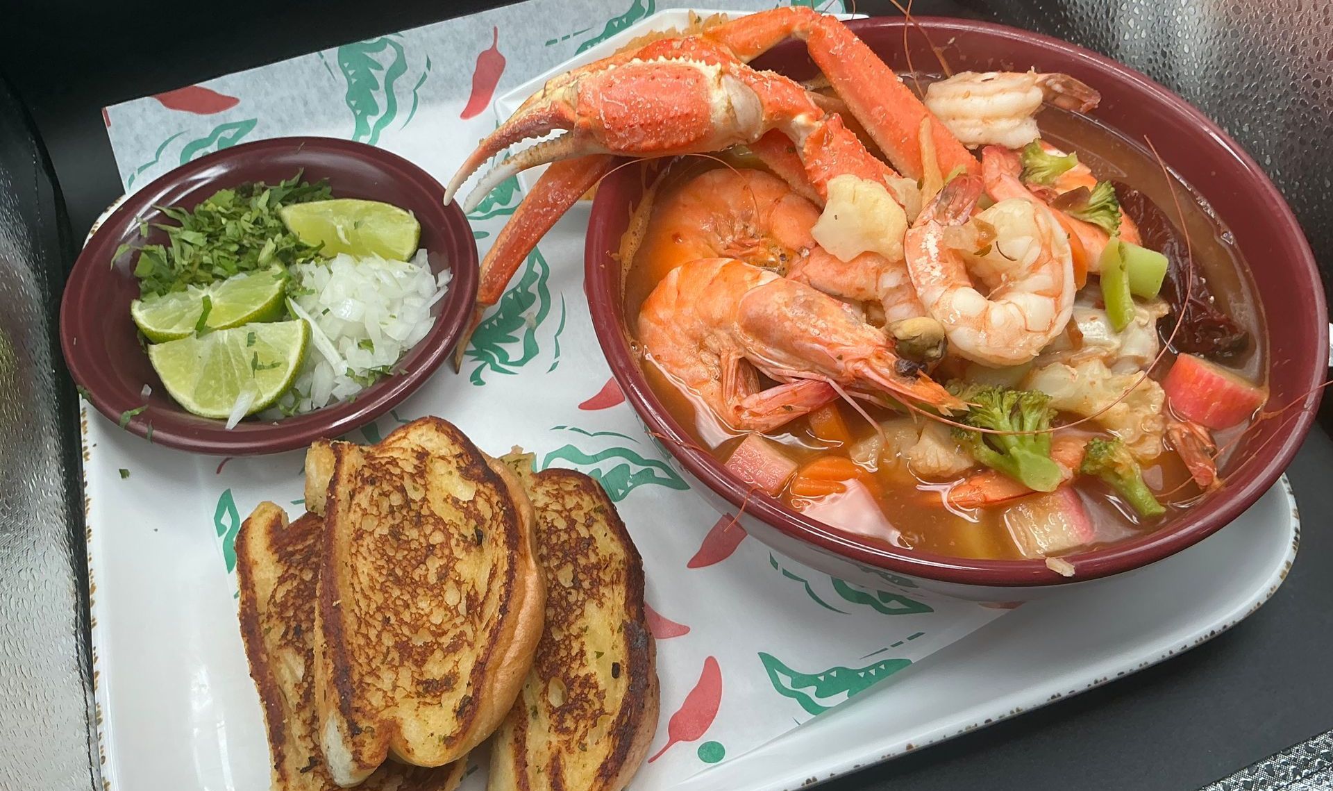 Seafood soup with shrimp, crab, and vegetables, served with toast and condiments on a tray.