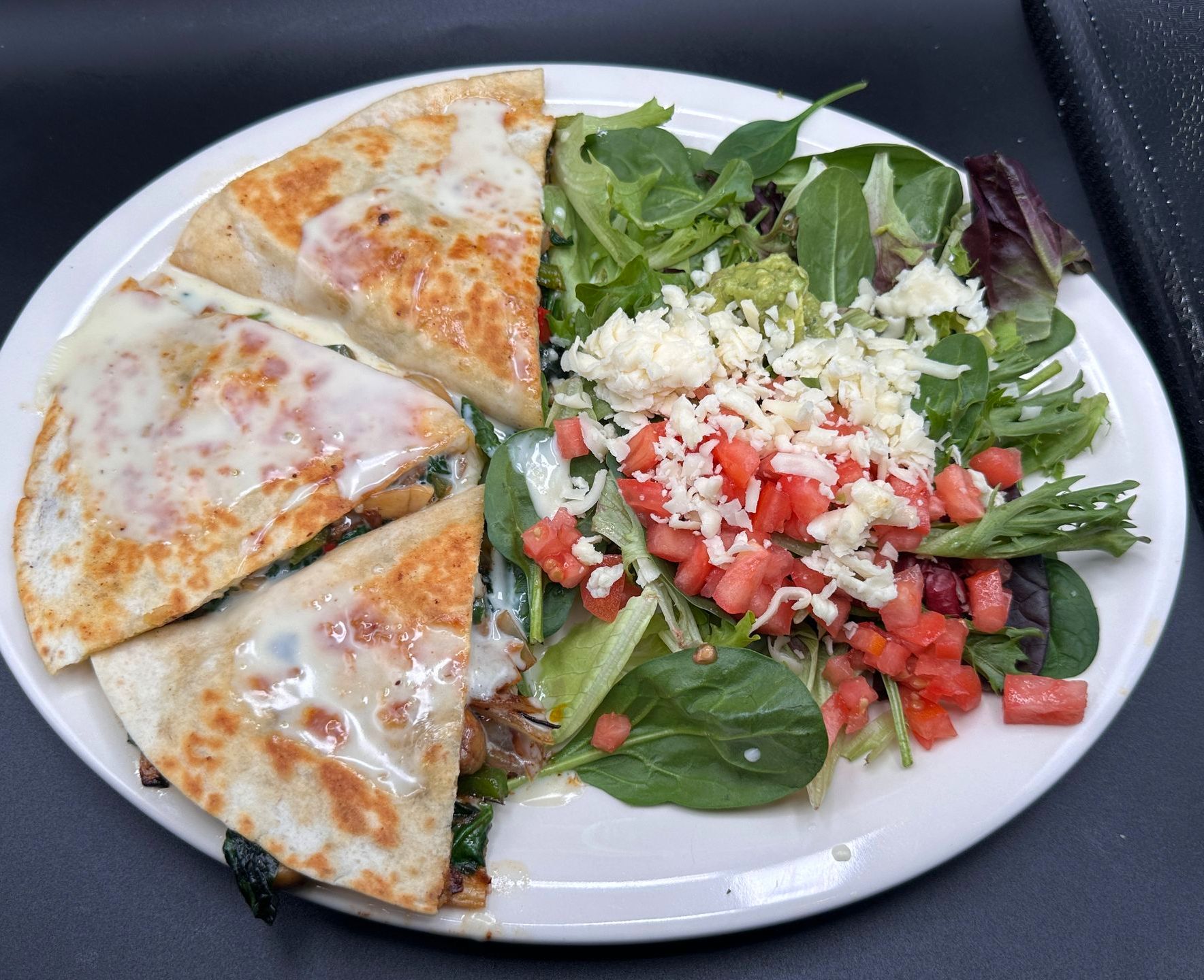 Quesadilla wedges and salad with guacamole, tomatoes, and cheese on a white plate.