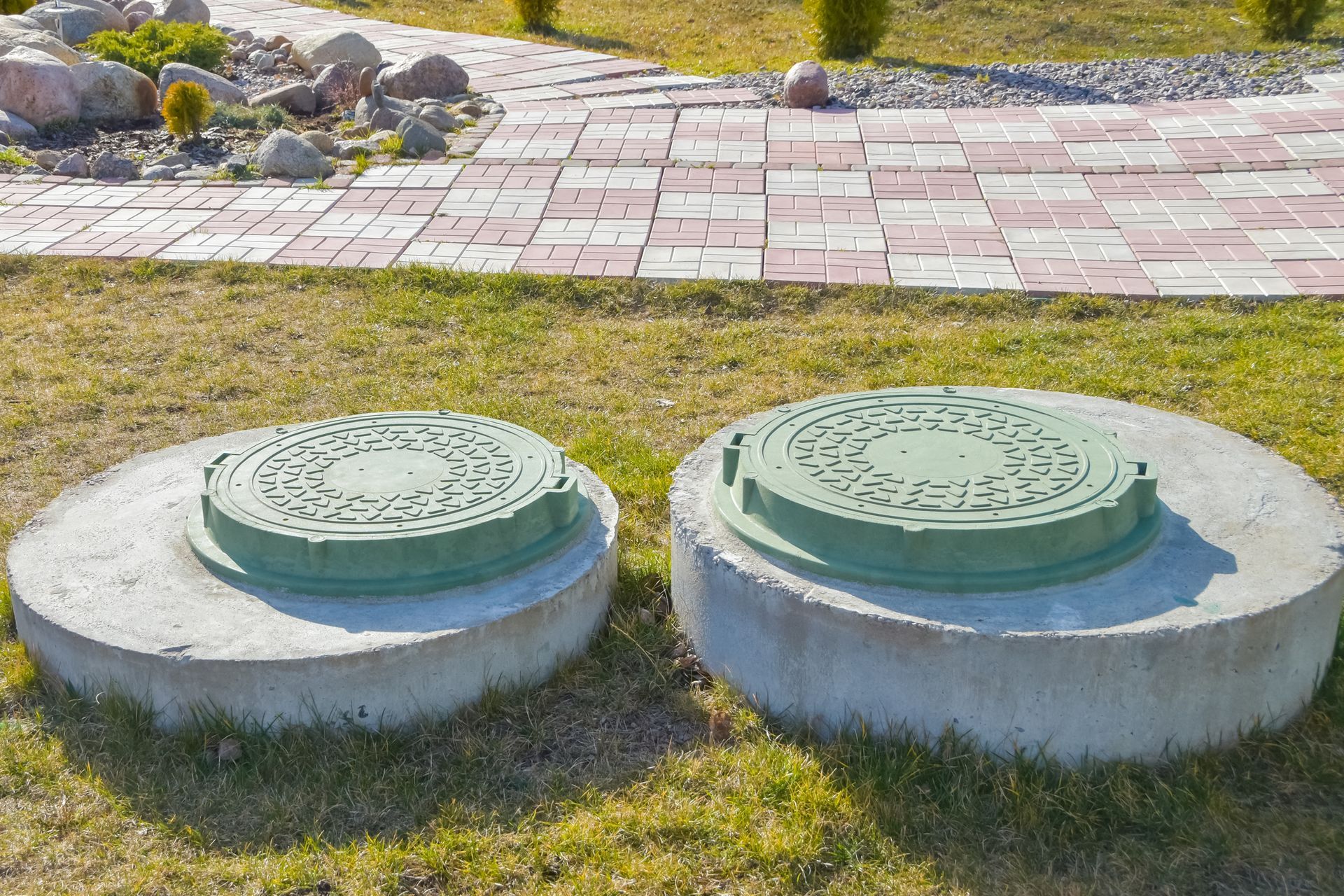 Two manhole covers on the grass outside a house, highlighting septic service in Greensboro, NC.