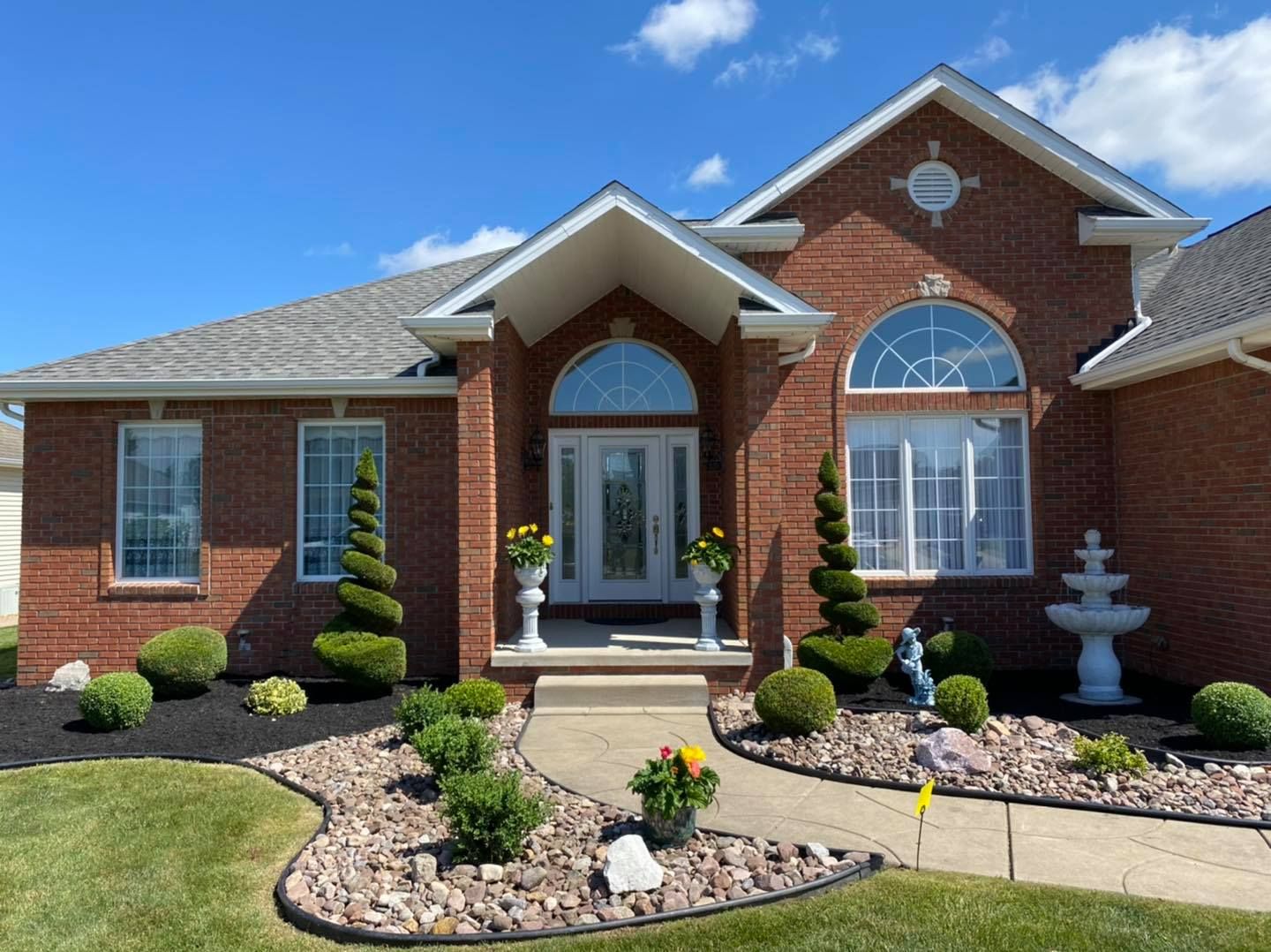 Brick suburban house with manicured front yard, arched windows, and stone walkway