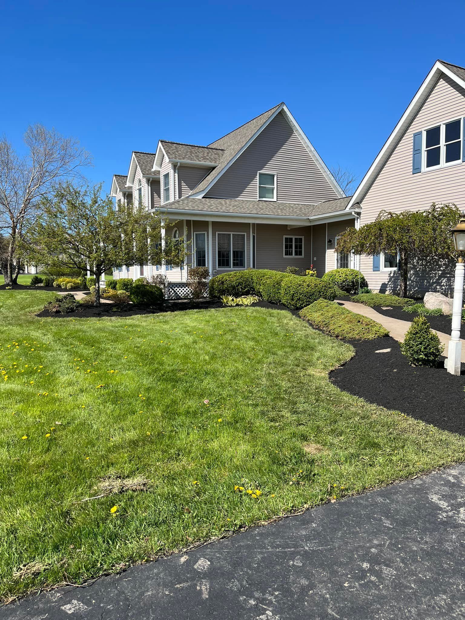 Suburban house with steep gables, green lawn, and a paved driveway under a clear blue sky