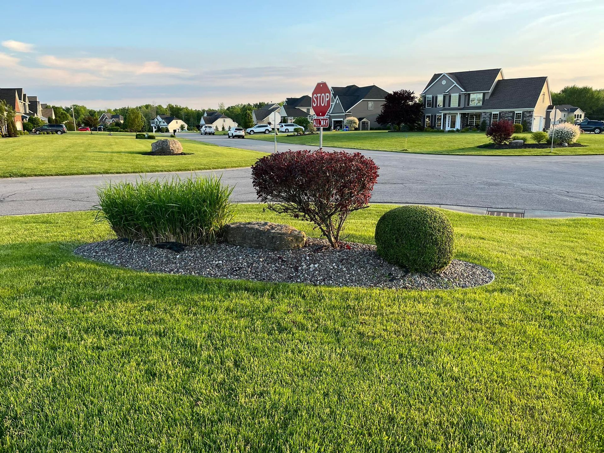 Suburban front yard with small shrubs and gravel bed beside a quiet street at sunset