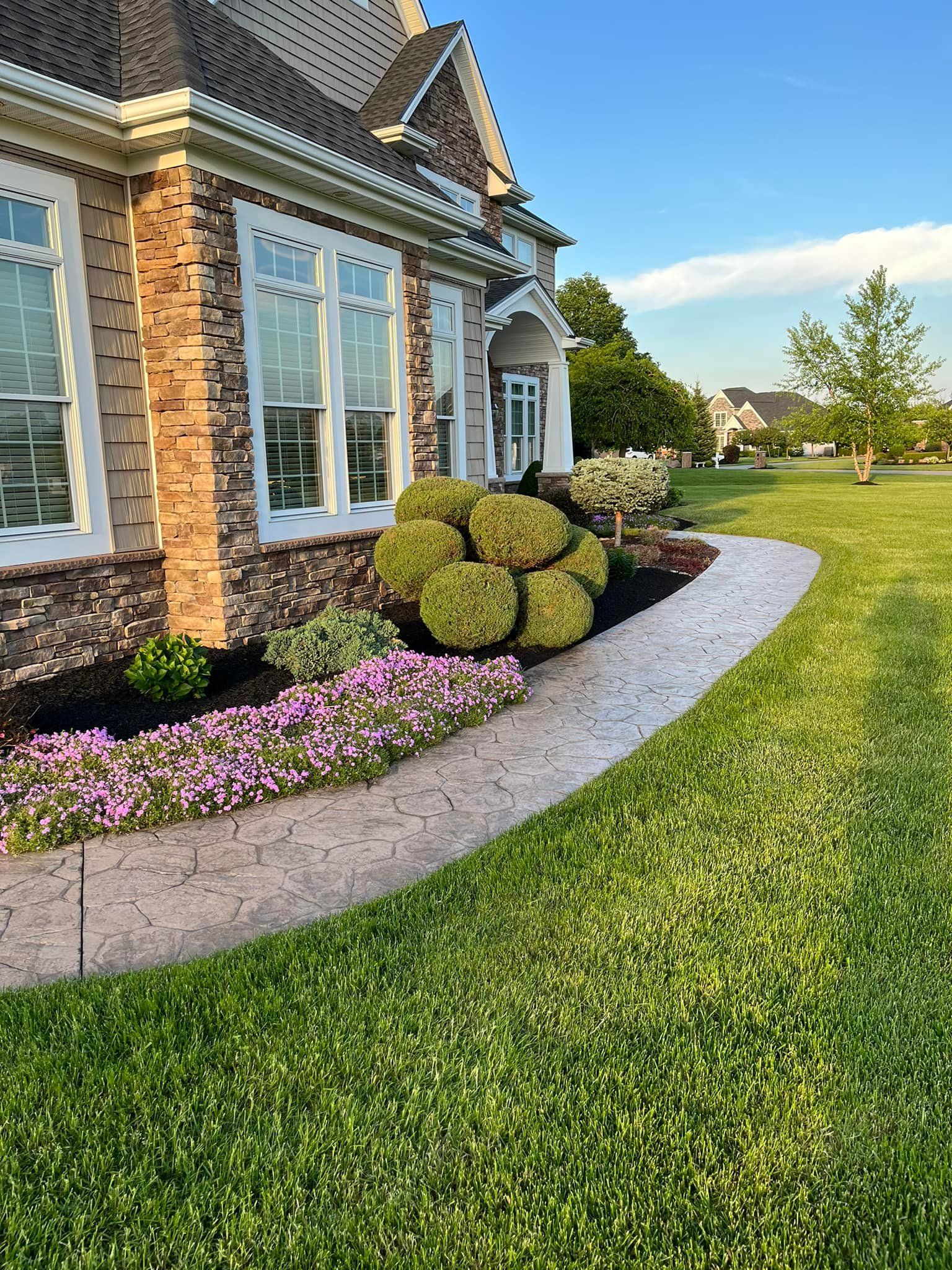 Brick house with manicured lawn, curved flower bed, and trimmed shrubs in the front yard.