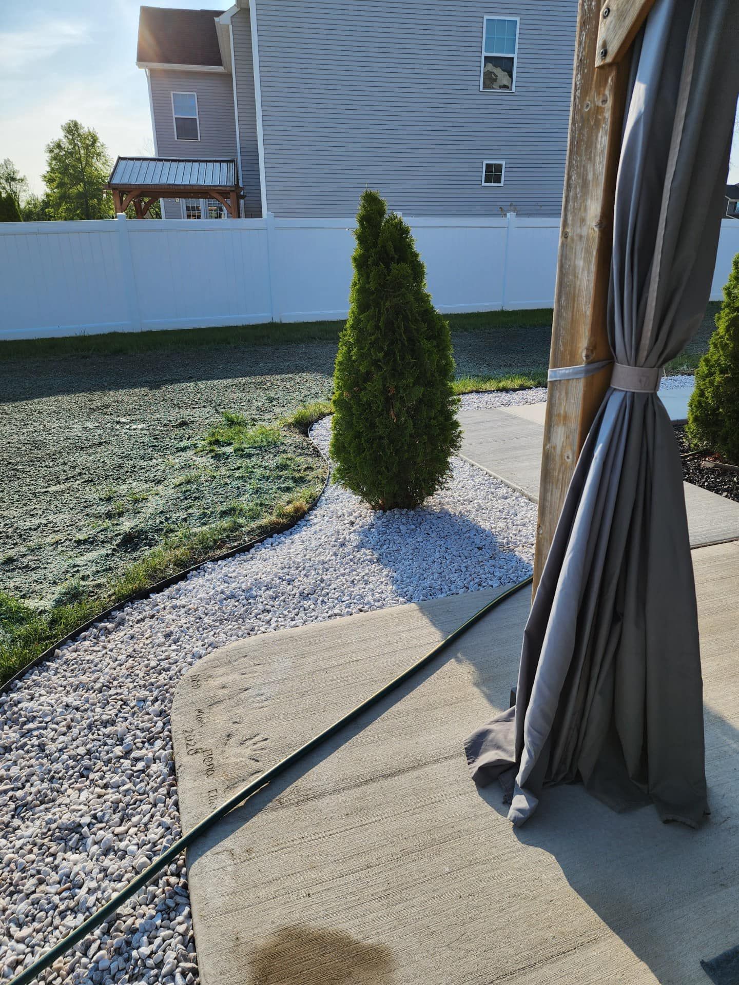 Backyard patio beside a gravel path, with a small evergreen shrub and a closed umbrella