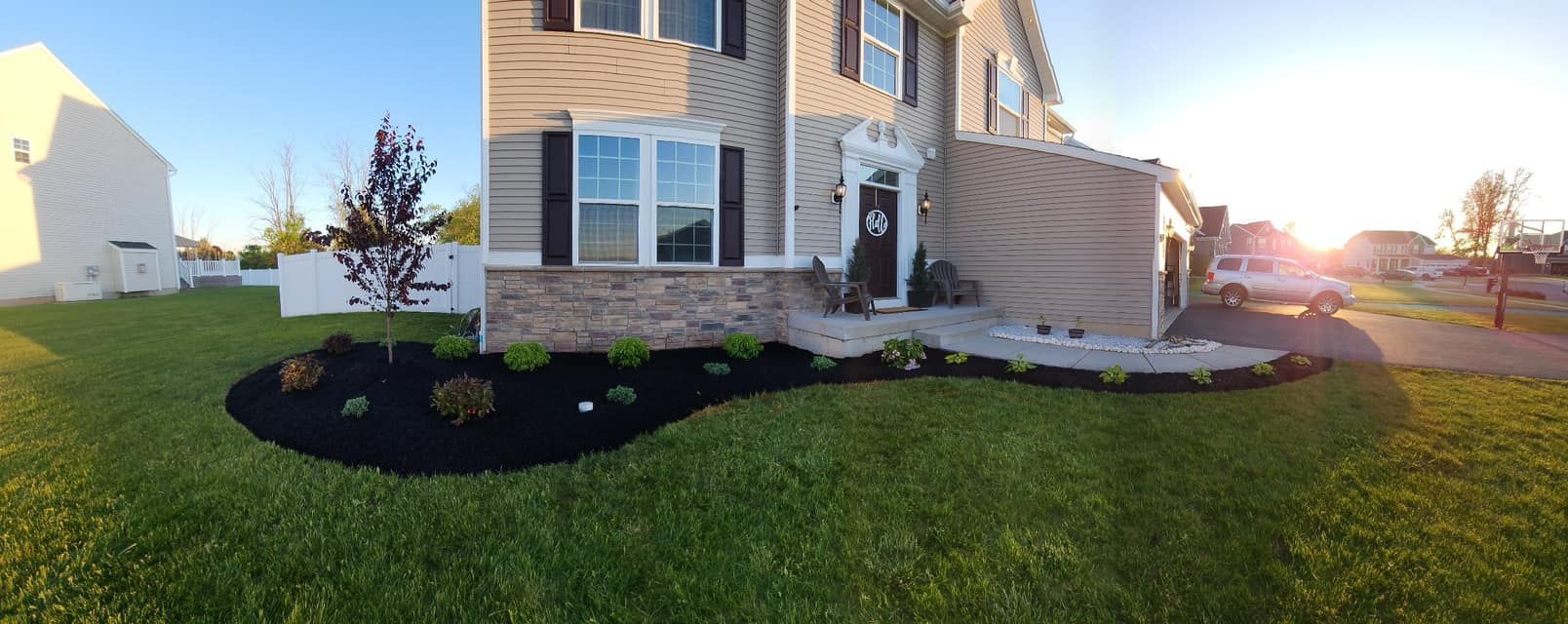 Suburban house front yard with lawn, mulch beds, and sunset light