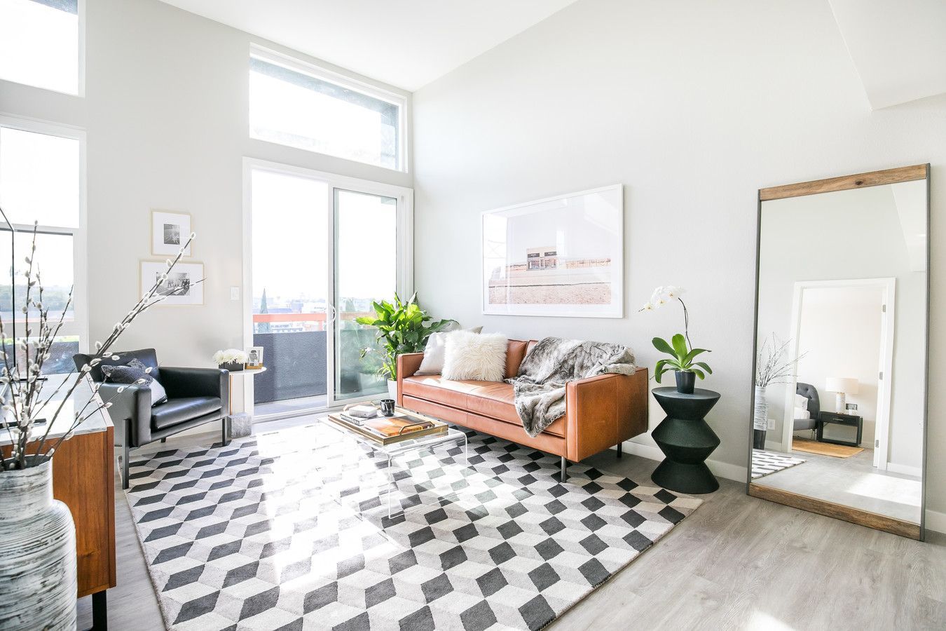 A bright, modern living room with a tan leather sofa, a geometric rug, and a large floor mirror.