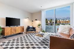 Modern living room with a brown leather couch, TV console, accent chair, patterned rug, and a balcony with mountain views.
