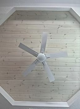 White ceiling fan on a light wood-paneled vaulted ceiling with white trim