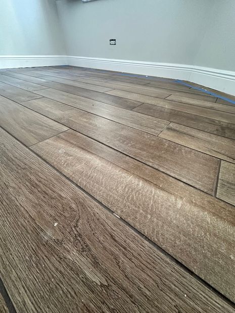 Empty room with unfinished wooden floor and white baseboards along a plain wall.