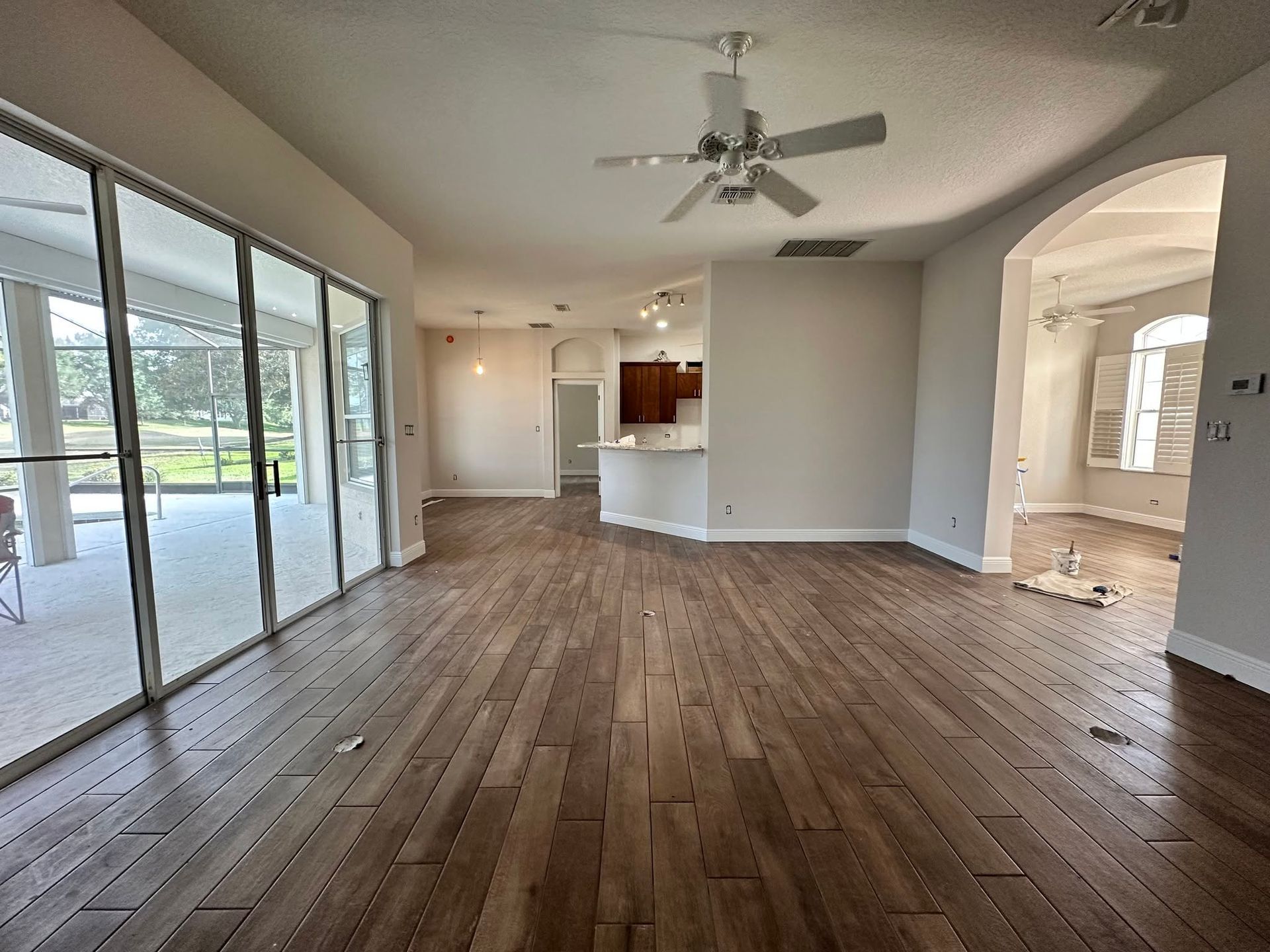 Empty open-plan living room with wood floors, ceiling fan, sliding glass doors, and kitchen pass-through