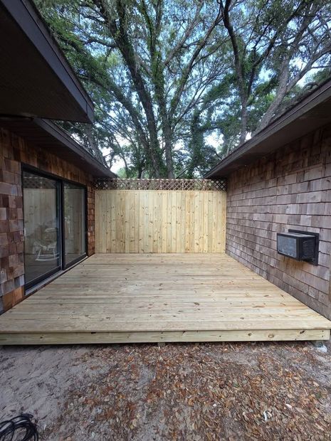Wooden deck between brick walls, with a light wood privacy fence at the end under tall trees.