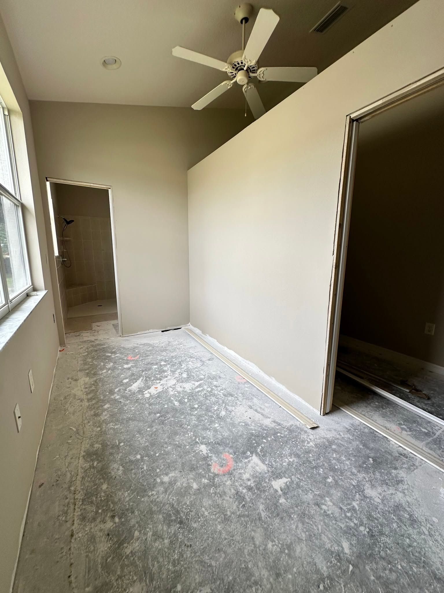 Empty beige room with ceiling fan, open doorway, and window light on carpeted floor.