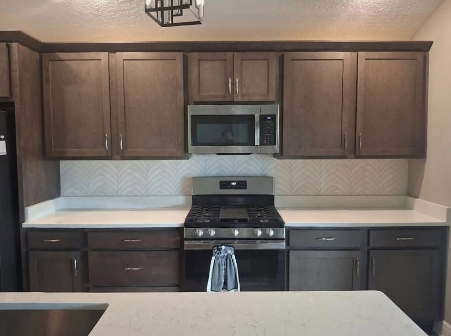 Modern kitchen with dark wood cabinets, white countertops, and stainless steel stove and microwave.