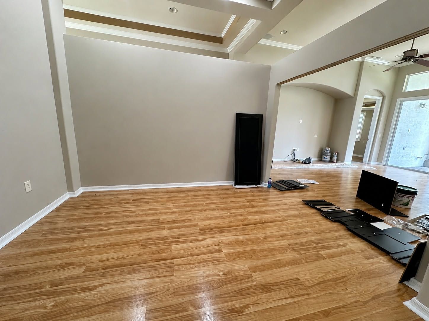 Empty living room with hardwood floors, beige walls, tray ceiling, and construction materials near the right wall