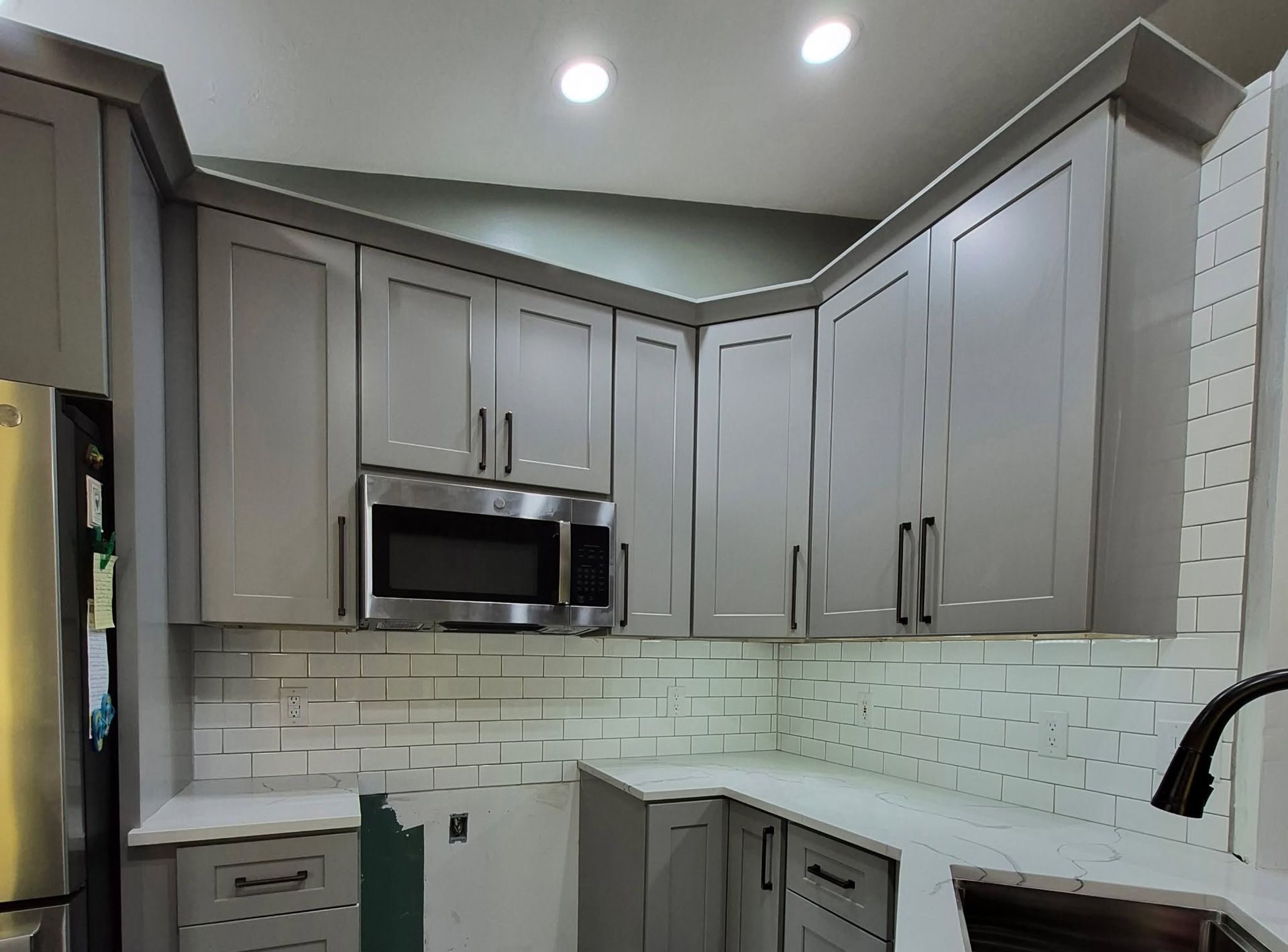 Modern kitchen with gray cabinets, white subway tile backsplash, and stainless steel microwave under recessed lights