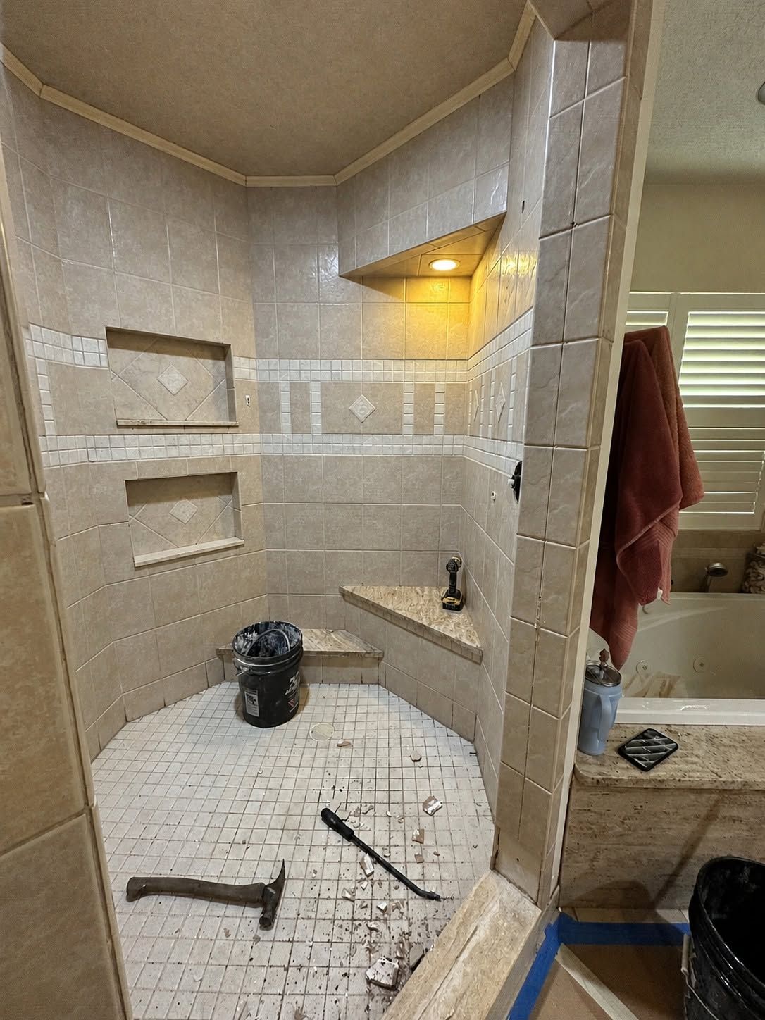 Tiled bathroom shower under renovation with white wall tiles, built-in niches, and tools on the floor