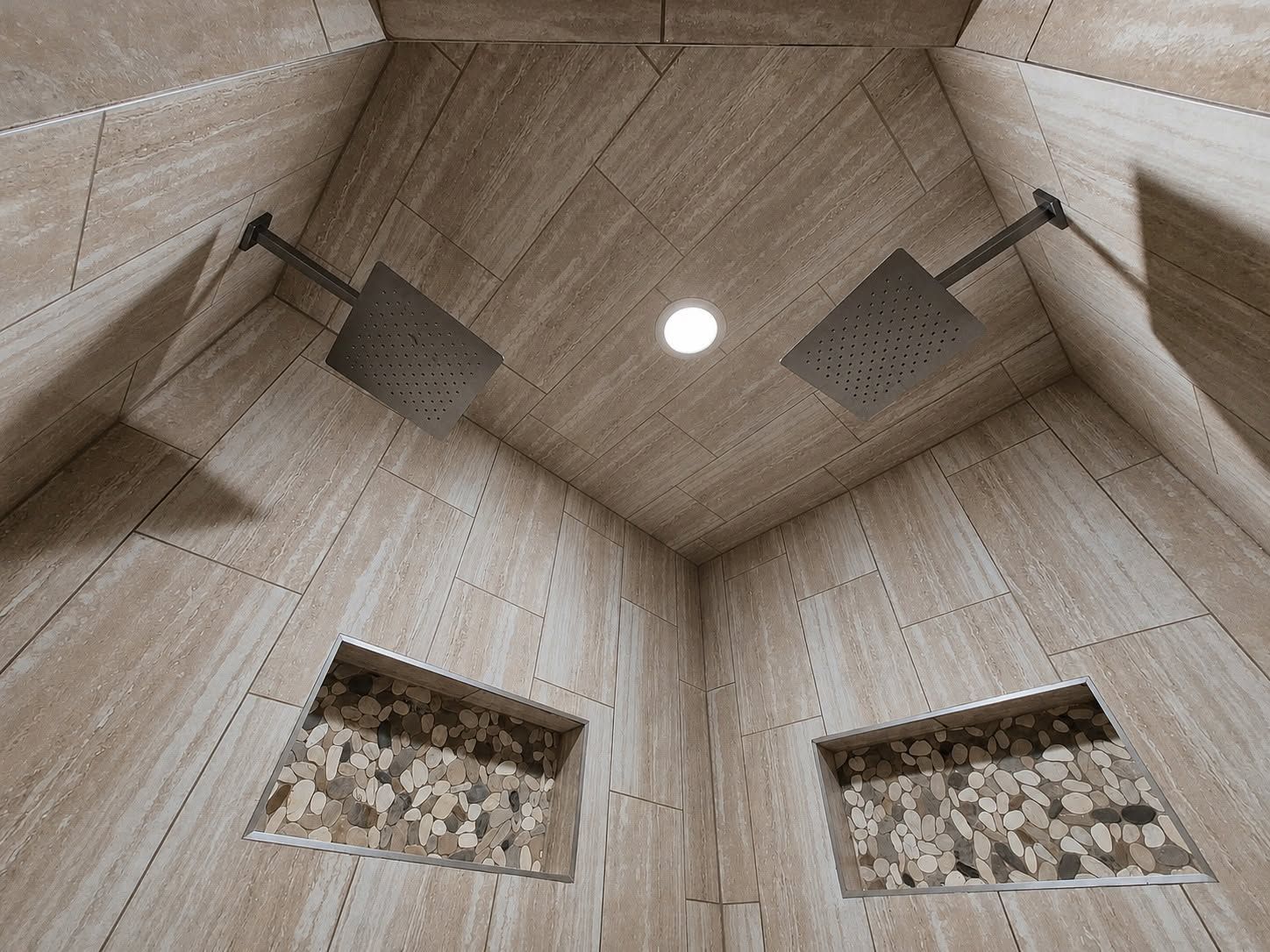 Stone-tiled shower ceiling with two showerheads and a round recessed light