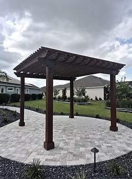 Wooden gazebo on a paved circular patio in a landscaped courtyard under cloudy skies