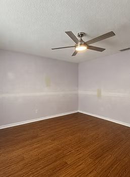Empty room with light gray walls, wood floor, and a ceiling fan light.