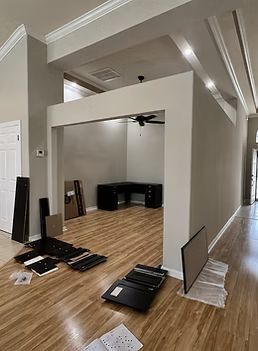 Empty room with wood floors, a white partition wall, and scattered furniture panels during setup