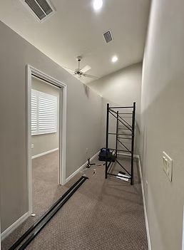 Narrow hallway under renovation with scaffolding, tools, and trim pieces on carpeted floor