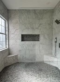 Marble-tiled shower with built-in benches, window, and pebble floor