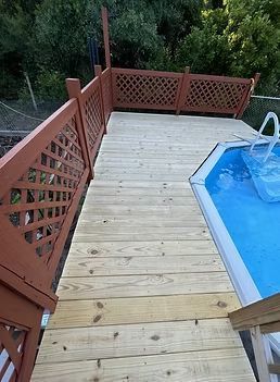 Wooden deck with red lattice railing beside an above-ground pool and surrounding trees