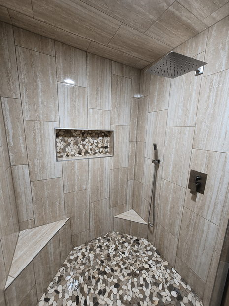 Empty tiled shower stall with a hexagonal floor, wall shelves, and beige stone-like walls