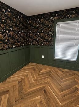 Empty room with dark floral wallpaper, green wainscoting, and herringbone wood floor.