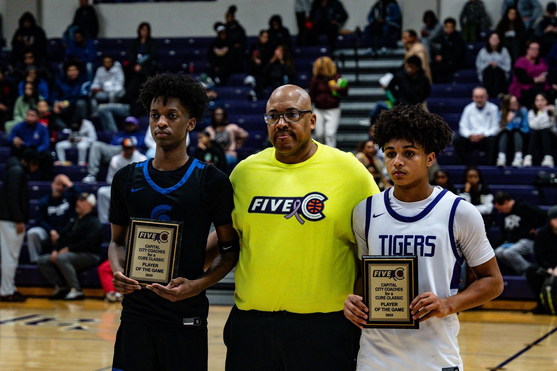 Two basketball players are standing next to each other and Coach Gohlson on a court holding plaques.