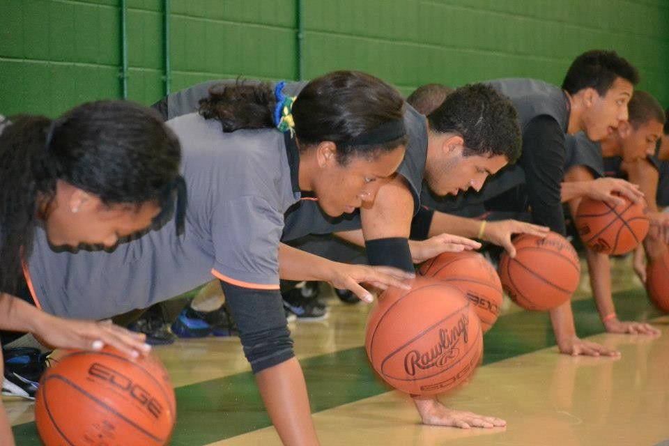 A group of people are doing push ups with basketballs on the floor.