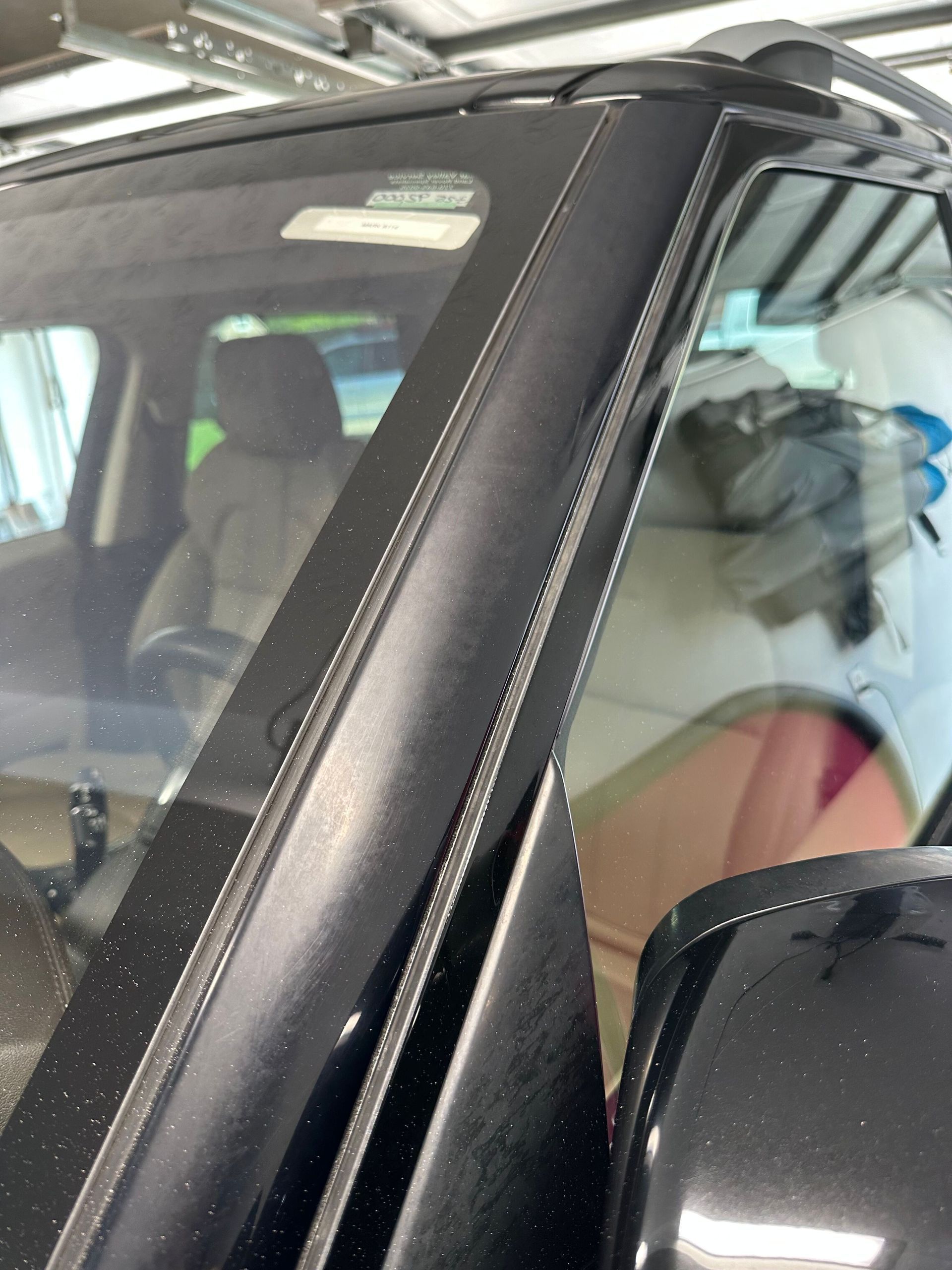Black car's windshield frame, showing seam details, reflections of interior, and side mirror.