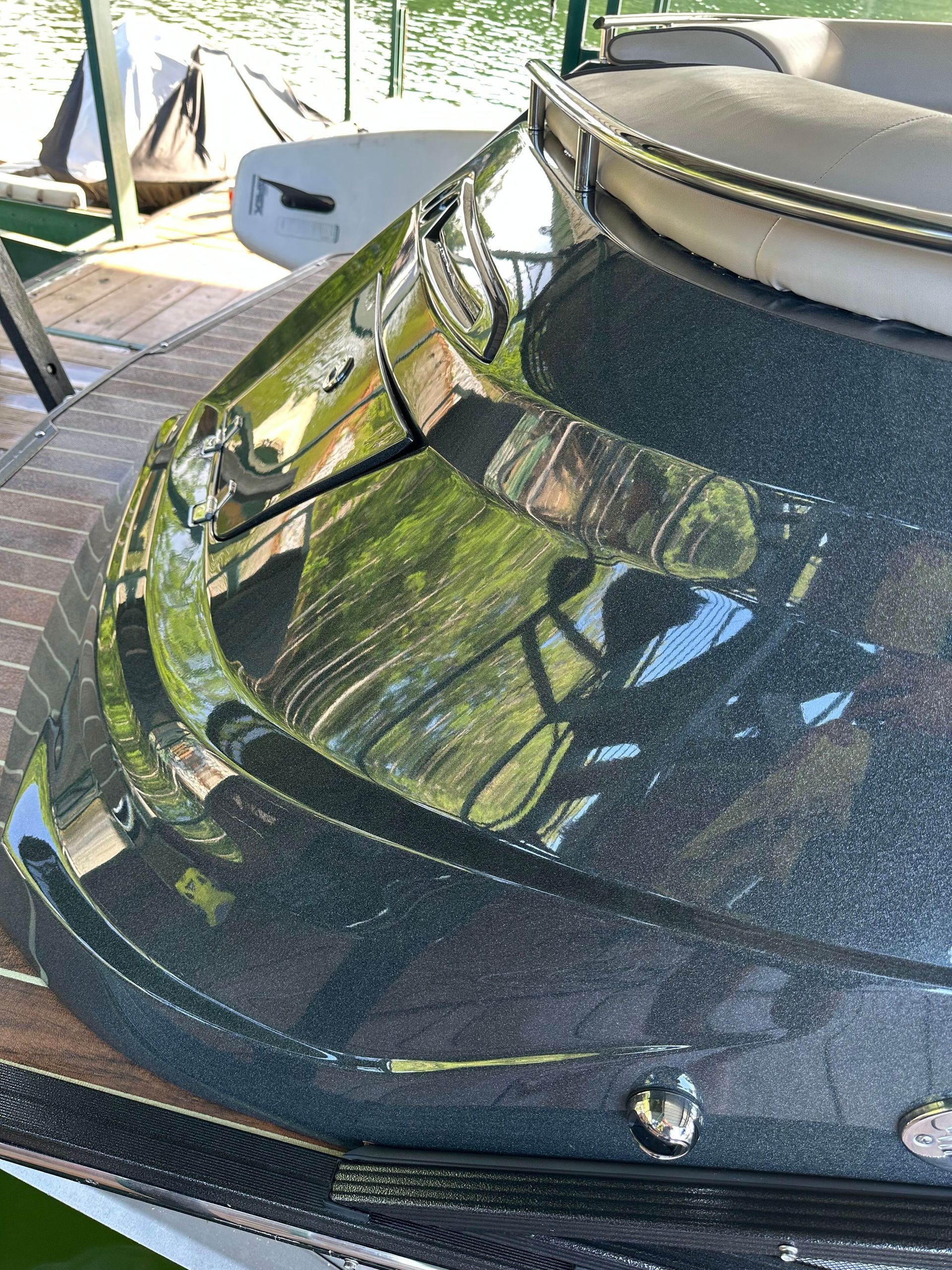 Dark green boat stern with chrome trim, reflecting trees and water.