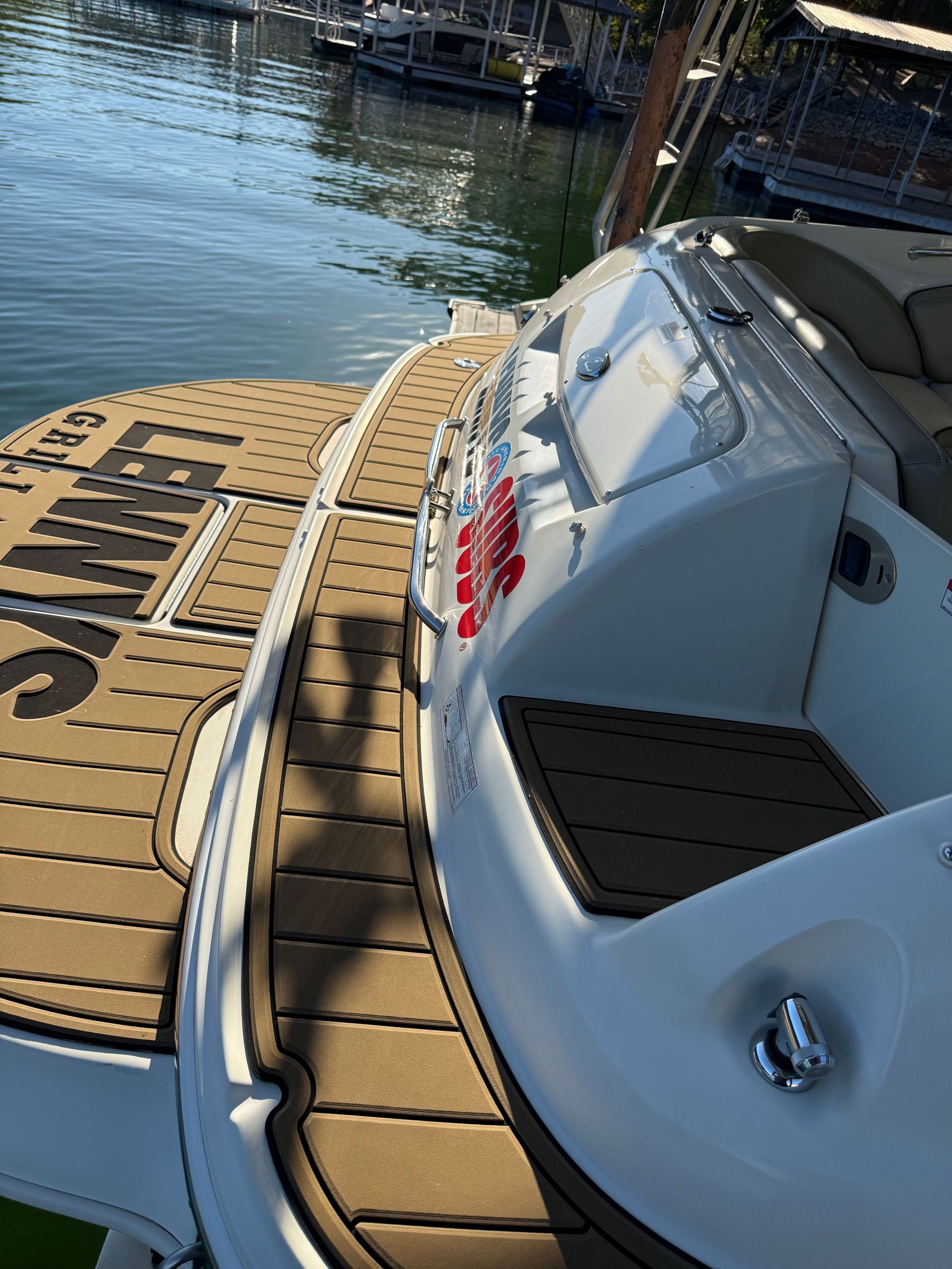 Brown and black boat decking on a white boat next to water; the boat reads